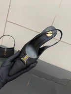 YSL black slingback pump held in gloved hand, close-up of strap and logo
