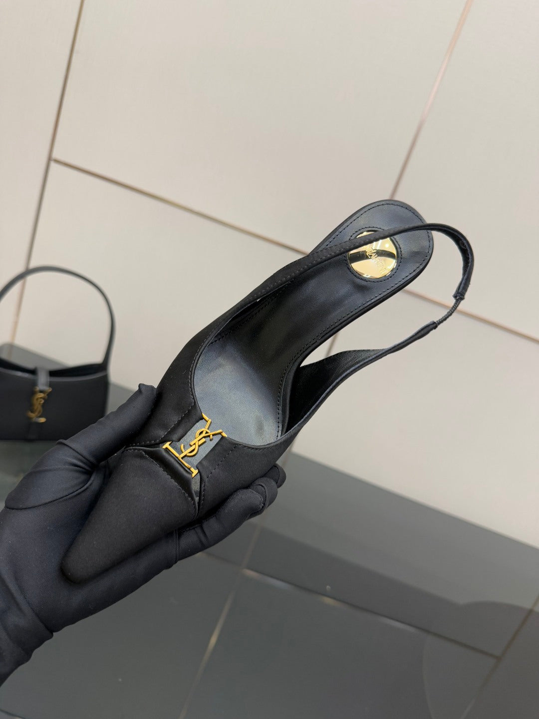 YSL black slingback pump held in gloved hand, close-up of strap and logo