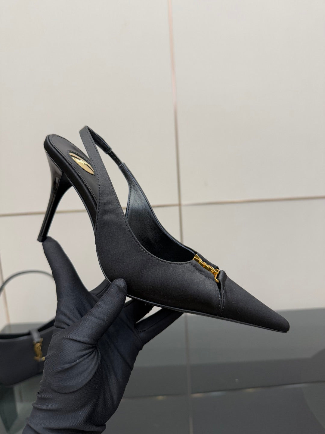 YSL black slingback pump held in gloved hand, pointed toe and gold logo