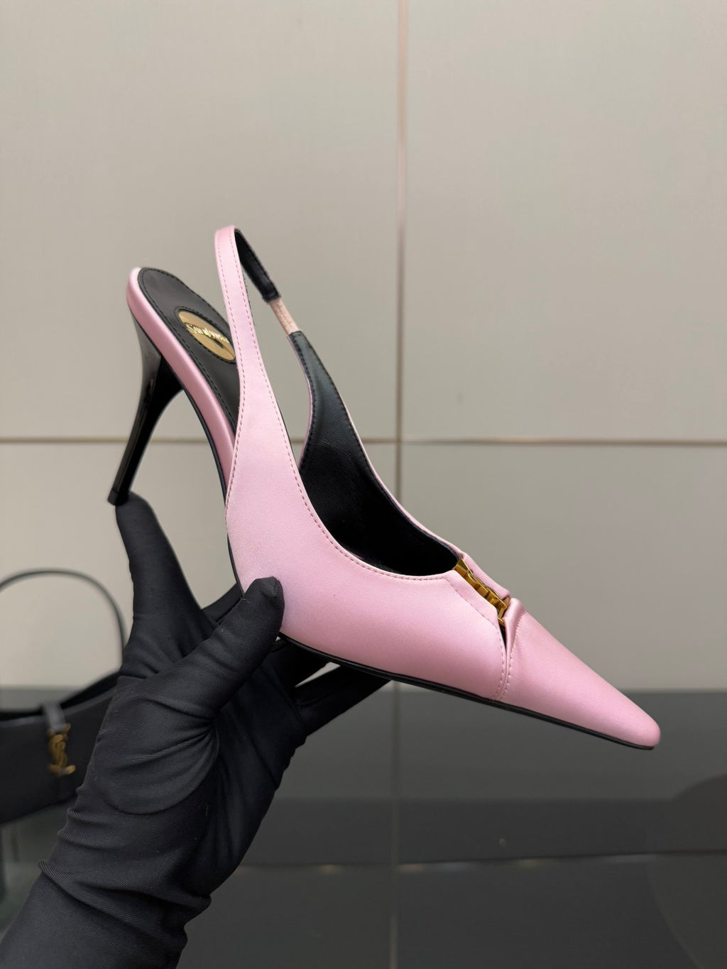 Pink leather pointed-toe slingback heel held in black-gloved hand; gold ankle detail