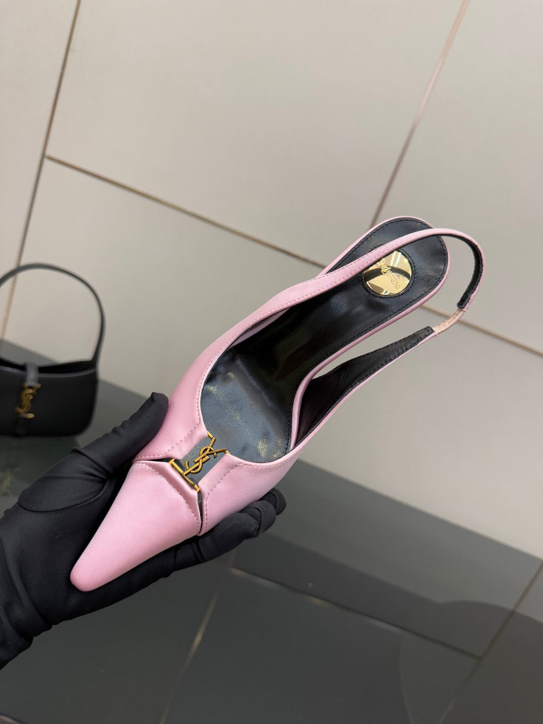 Pink slingback shoe in hand with black insole and gold logo at ankle strap
