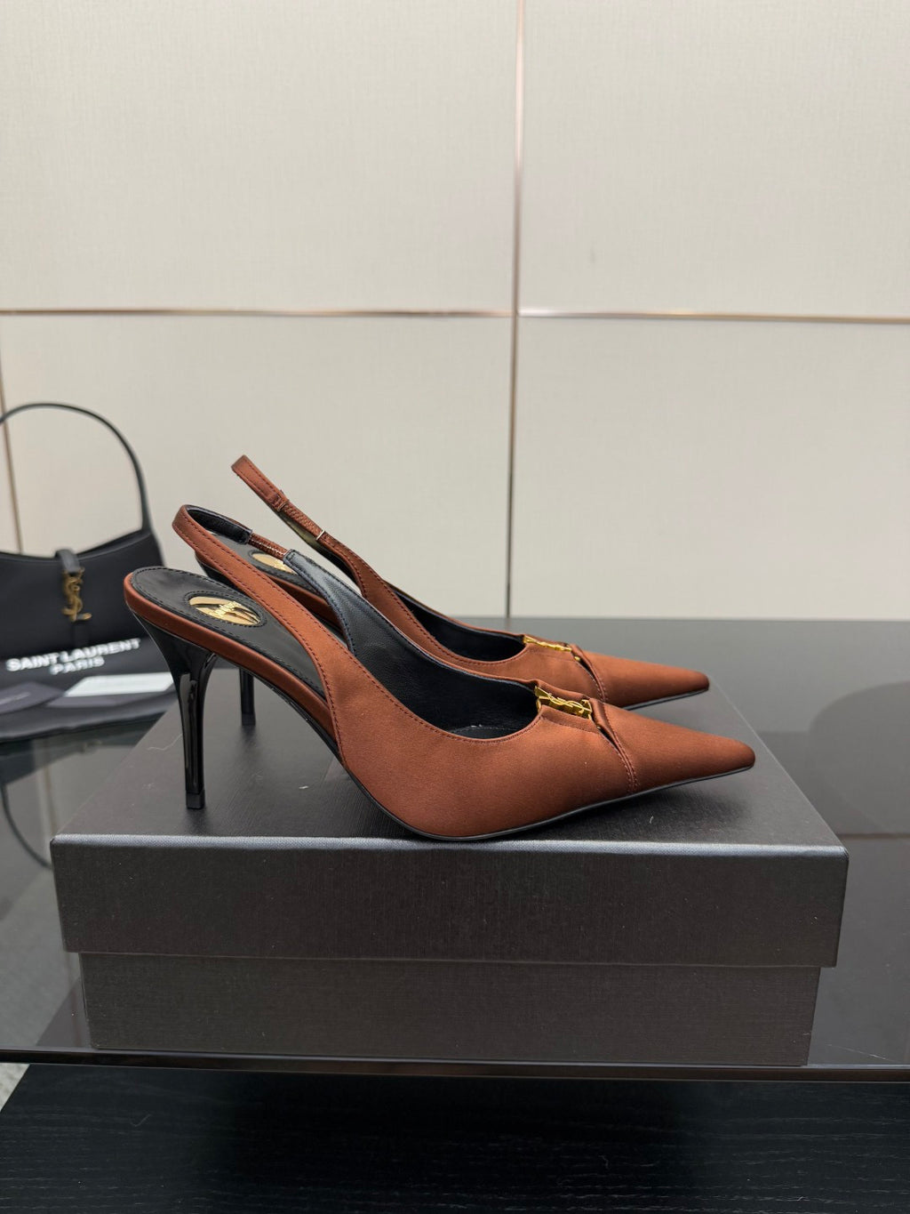 Tan leather slingback pump with thin stiletto heel and gold emblem on toe strap