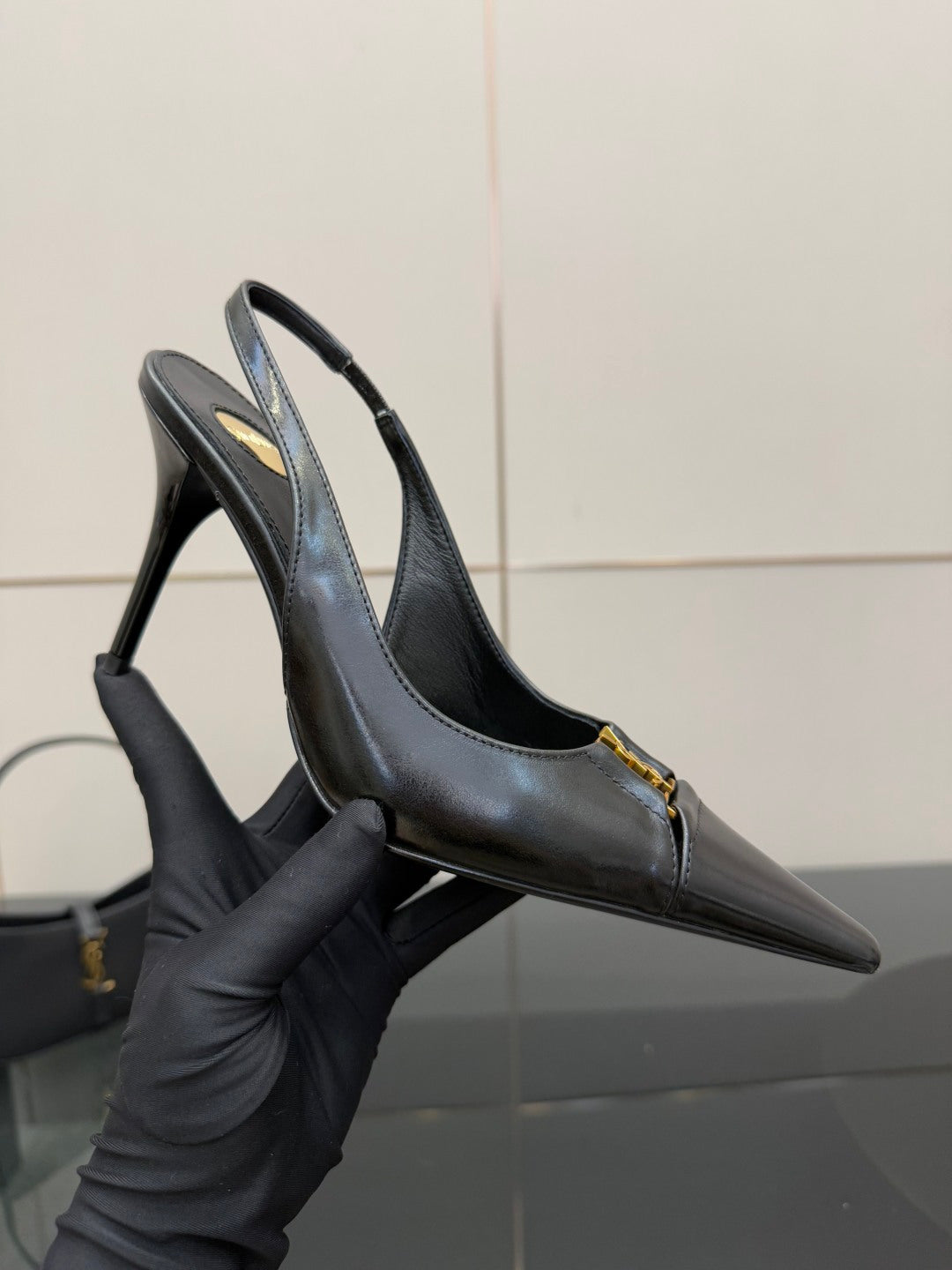 YSL ladies black leather pumps held in hand, pointed toe and gold logo detail