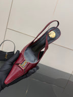 Burgundy red pointed-toe stiletto pump with gold logo detail on side, held close-up