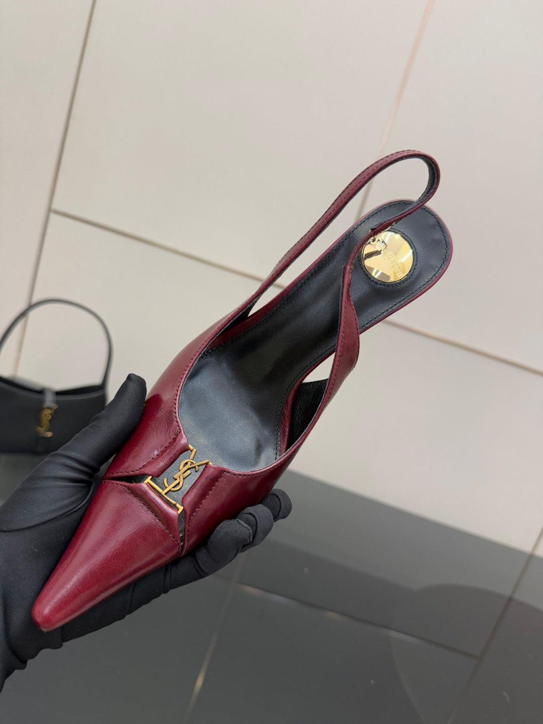 Burgundy red pointed-toe stiletto pump with gold logo detail on side, held close-up