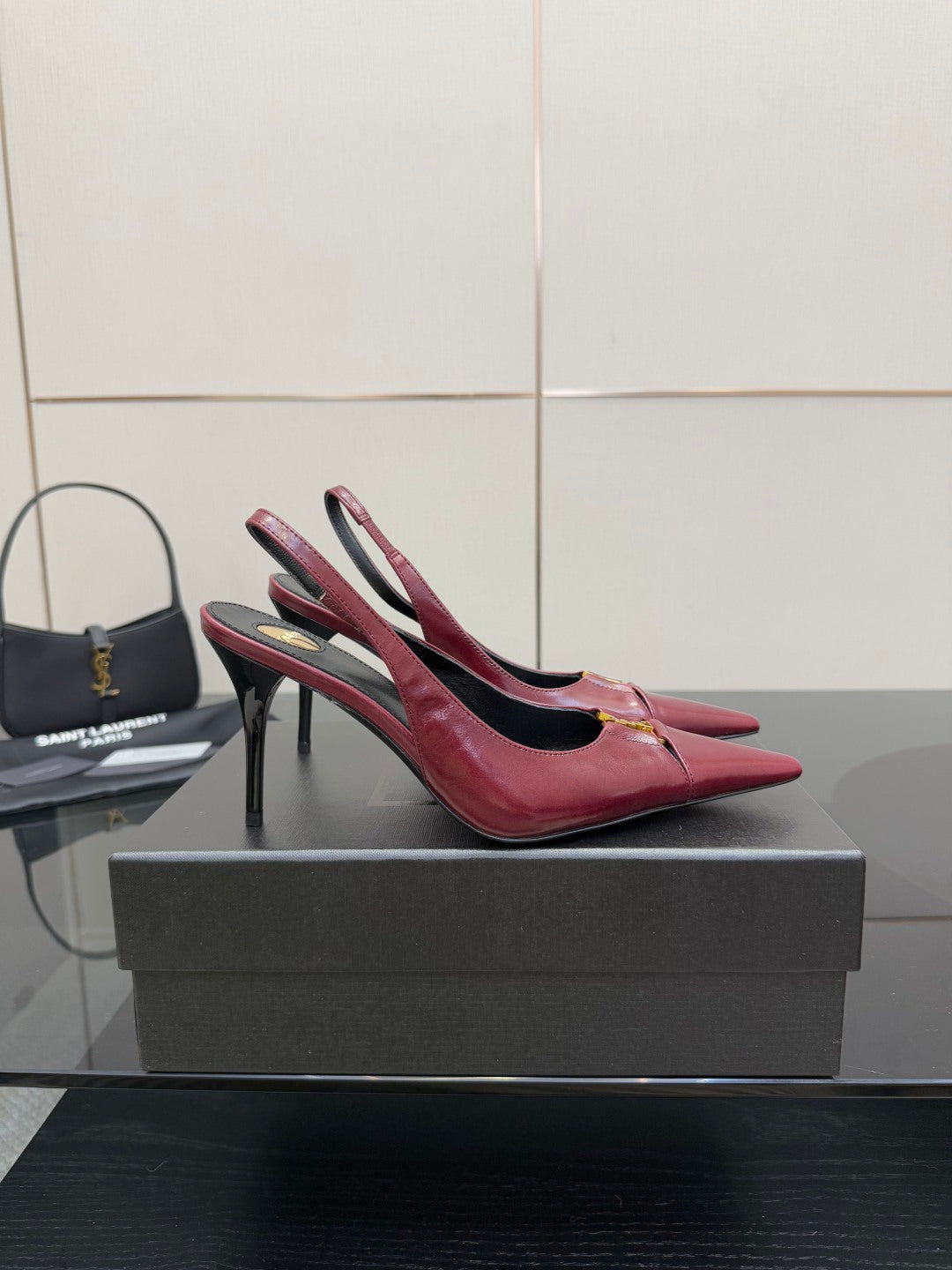 Burgundy red pointed-toe stiletto heel pair with ankle straps and gold emblem