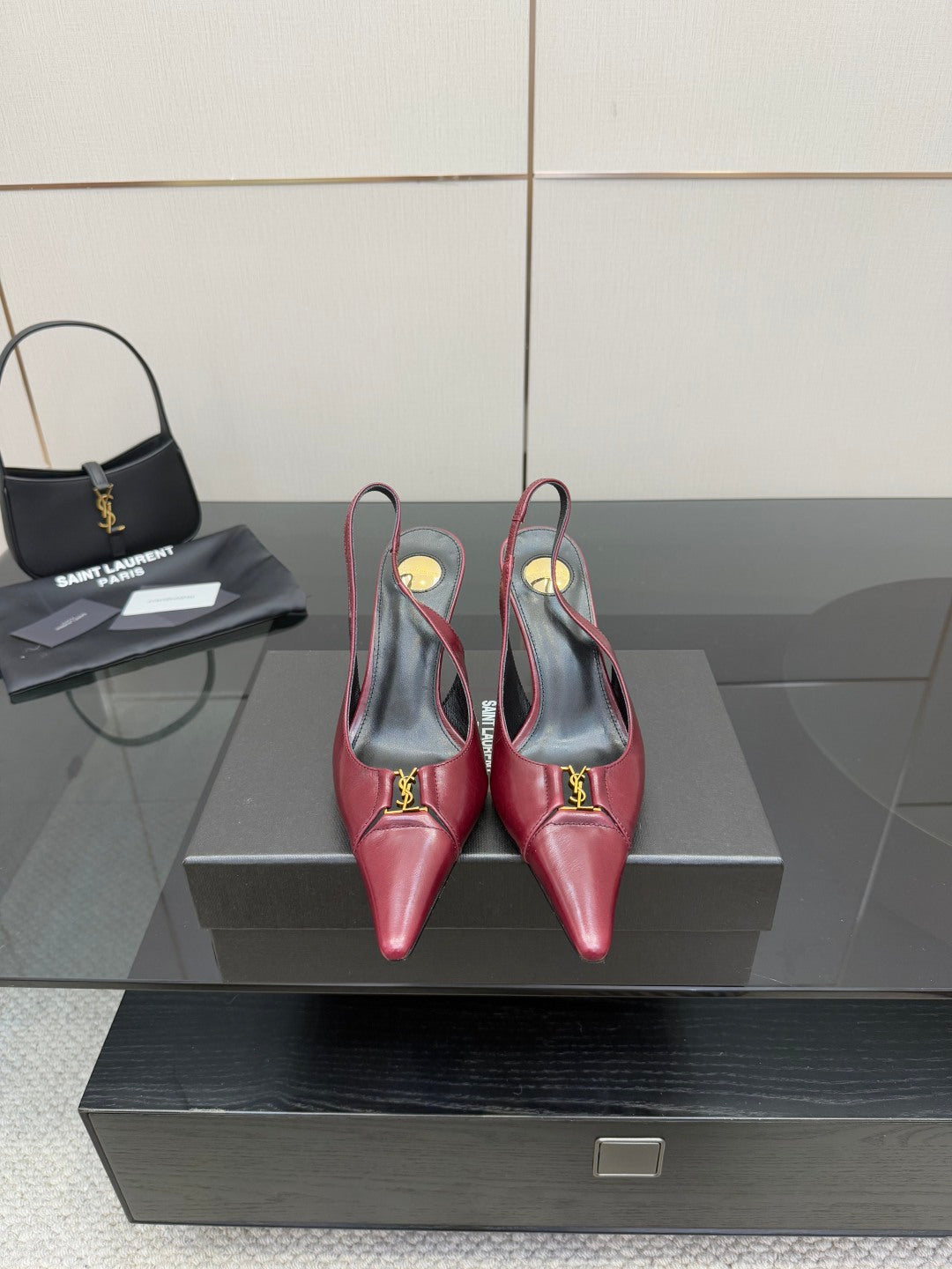Burgundy red pointed-toe stiletto heels with gold logo detail, on display pair