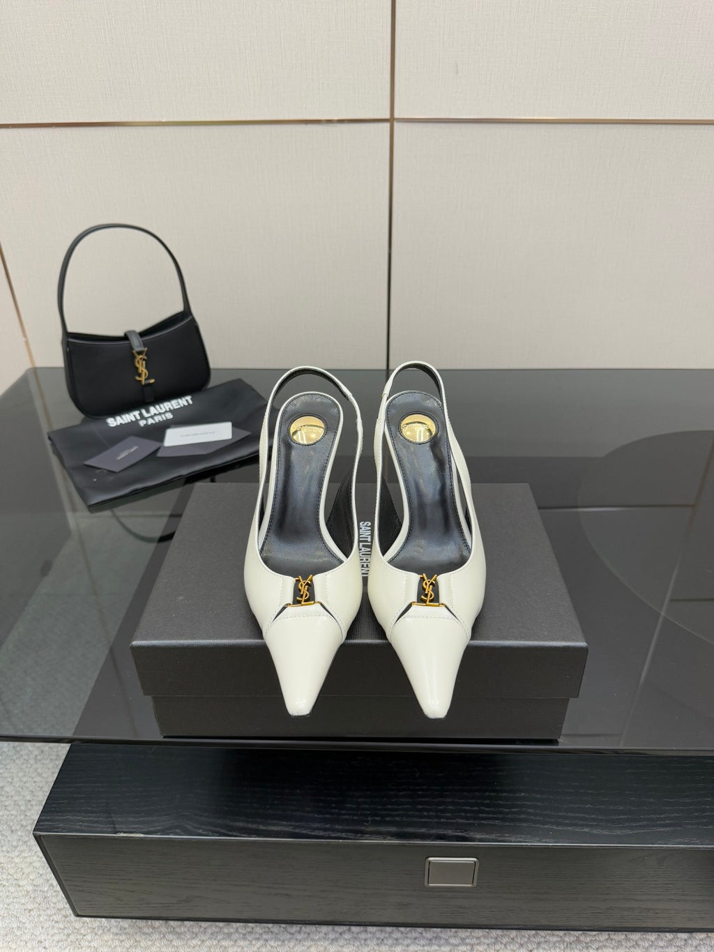 White pointed-toe slingback heels with black lining and gold logo detail, on display.