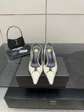 White pointed-toe slingback heels with black lining and gold logo detail, on display.