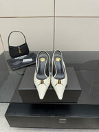 White pointed-toe slingback heels with black lining and gold logo detail, on display.