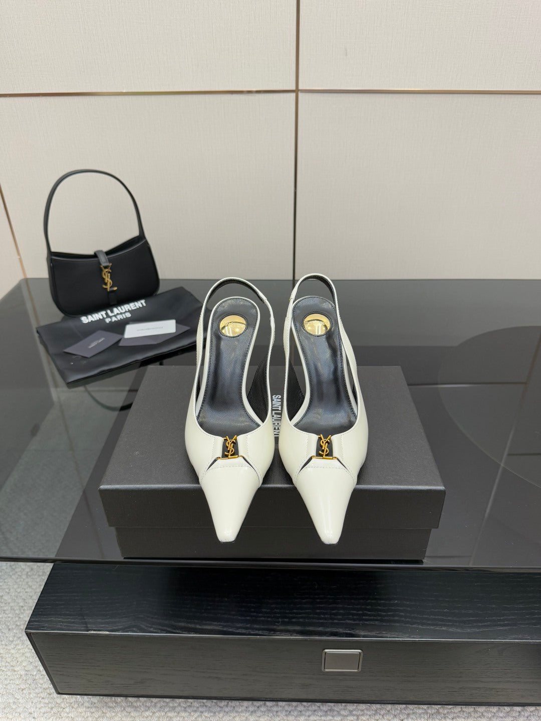 White pointed-toe slingback heels with black lining and gold logo detail, on display.