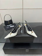 White pointed-toe slingback stiletto heels with black lining and small gold logo.