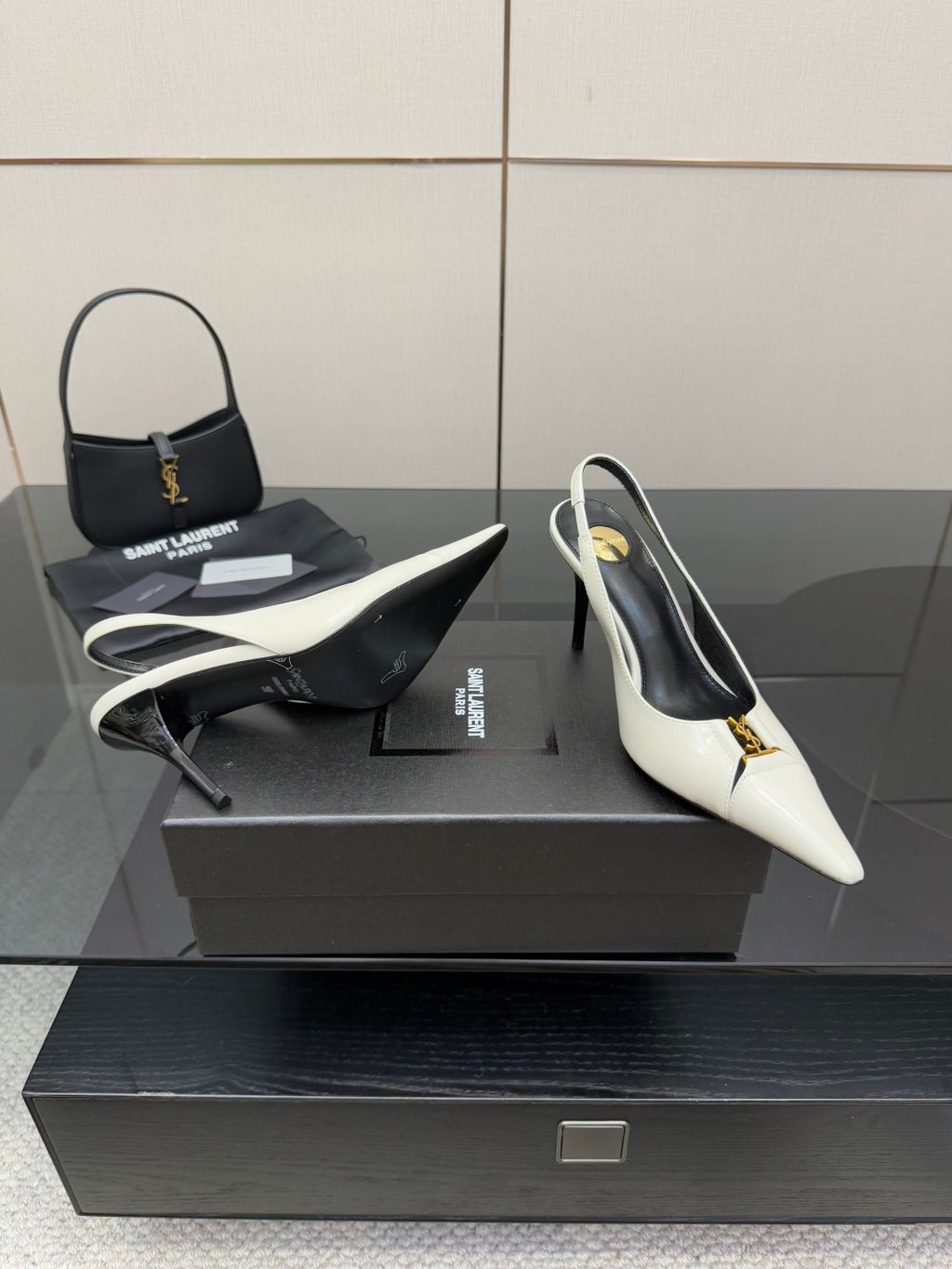 White pointed-toe slingback heels with black lining and gold logo accent, side view.