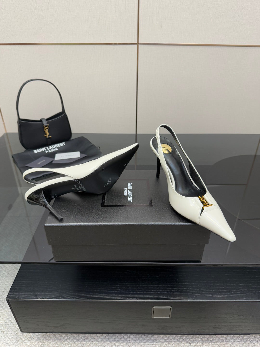 White pointed-toe slingback heels with black lining and gold logo accent, side view.