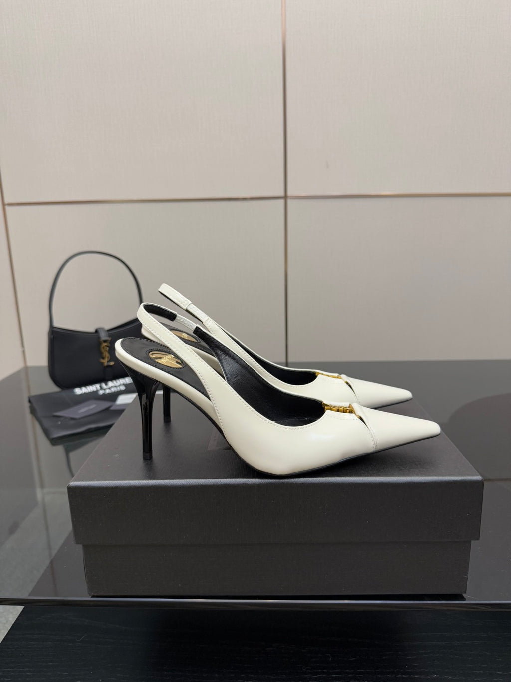 White pointed-toe slingback stiletto heels with black interior and gold logo hardware.