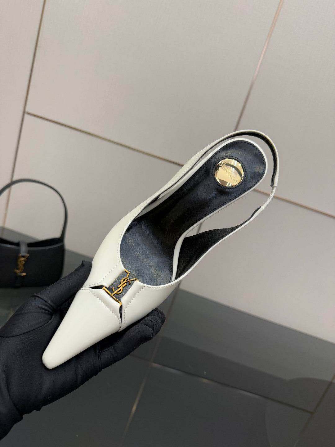 White slingback heel shoe opening with gold logo emblem and black lining, held up.