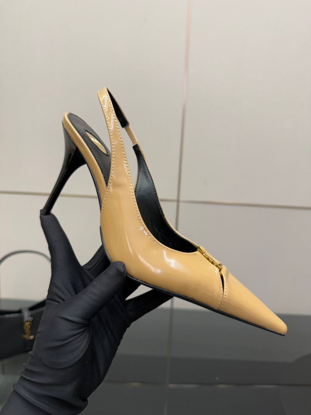 YSL beige patent slingback heel in gloved hand, pointed toe and stiletto heel