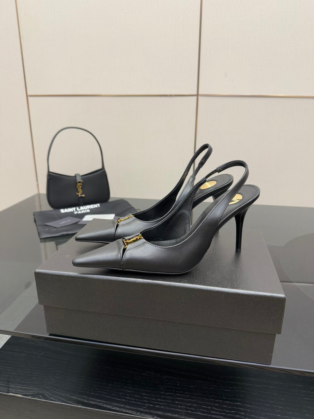Black pointed-toe stiletto pumps with gold logo trim, side view on display.