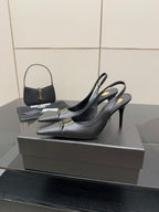 Black pointed-toe stiletto pumps with gold logo trim, side view on display.