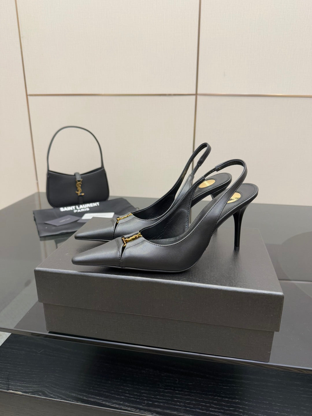 Black pointed-toe stiletto pumps with gold logo trim, side view on display.