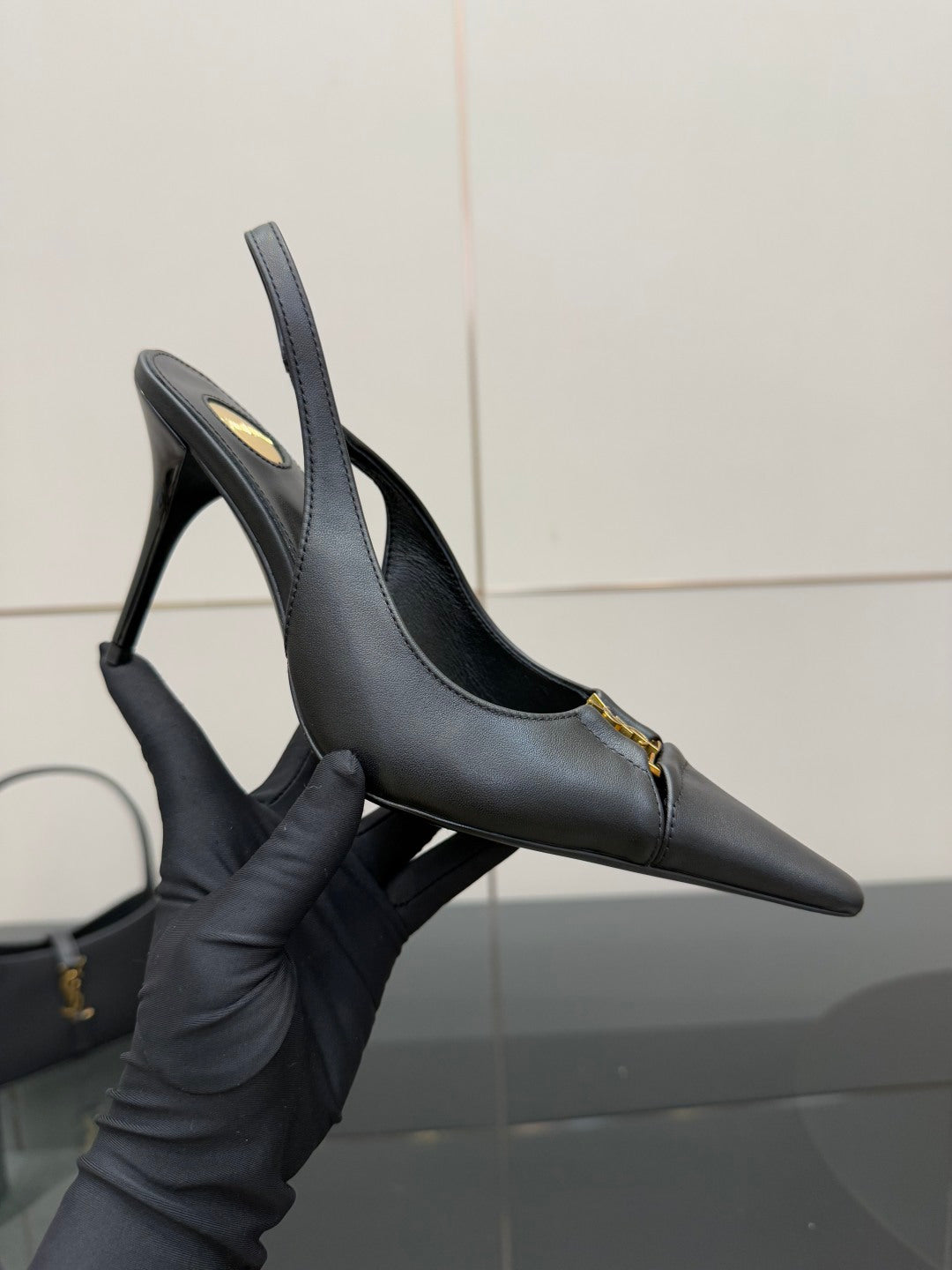 Black stiletto pumps with pointed toe and gold logo detail, held for close view.