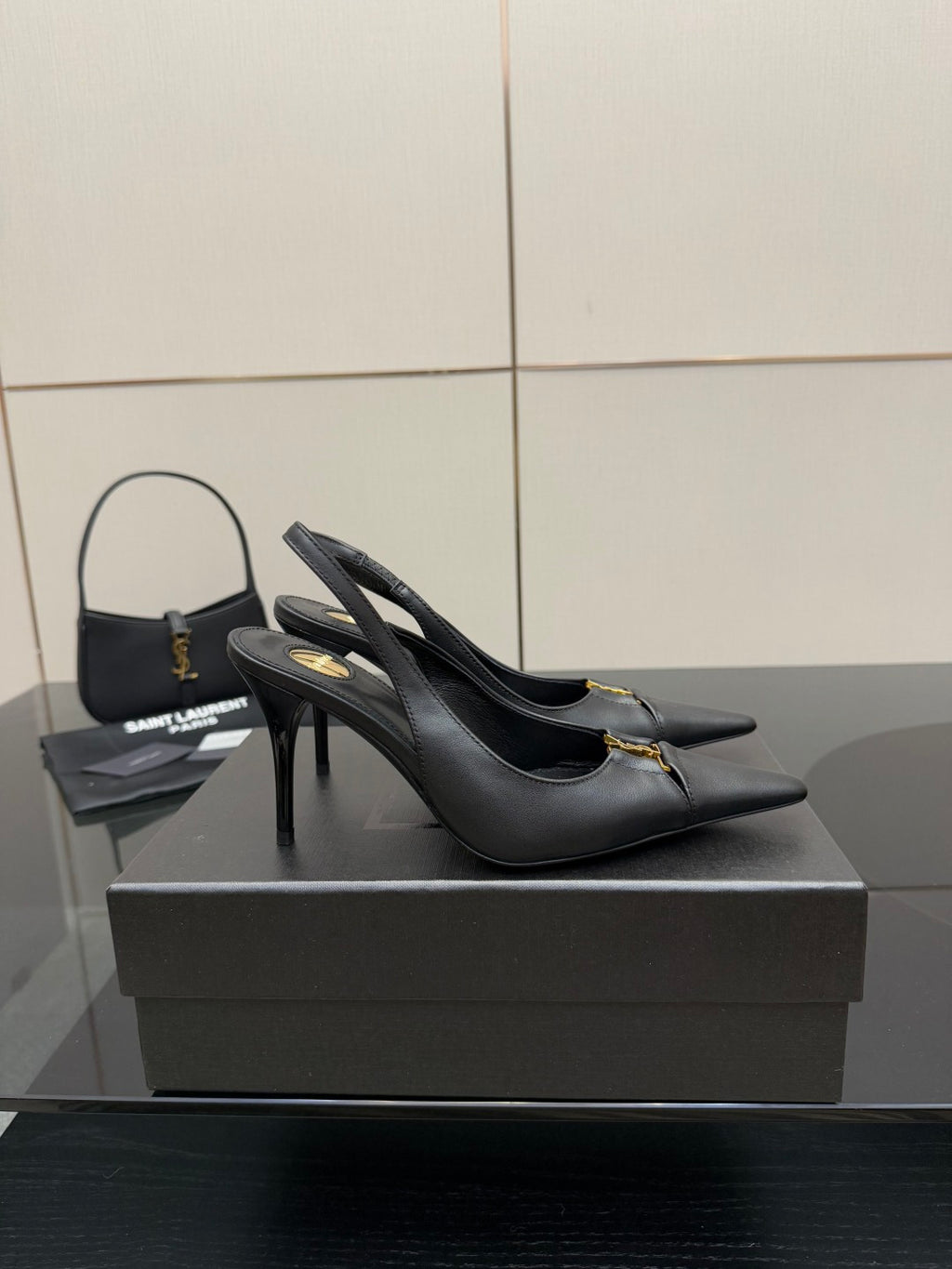 Black slingback stiletto pumps with gold logo detail, angled view on display.