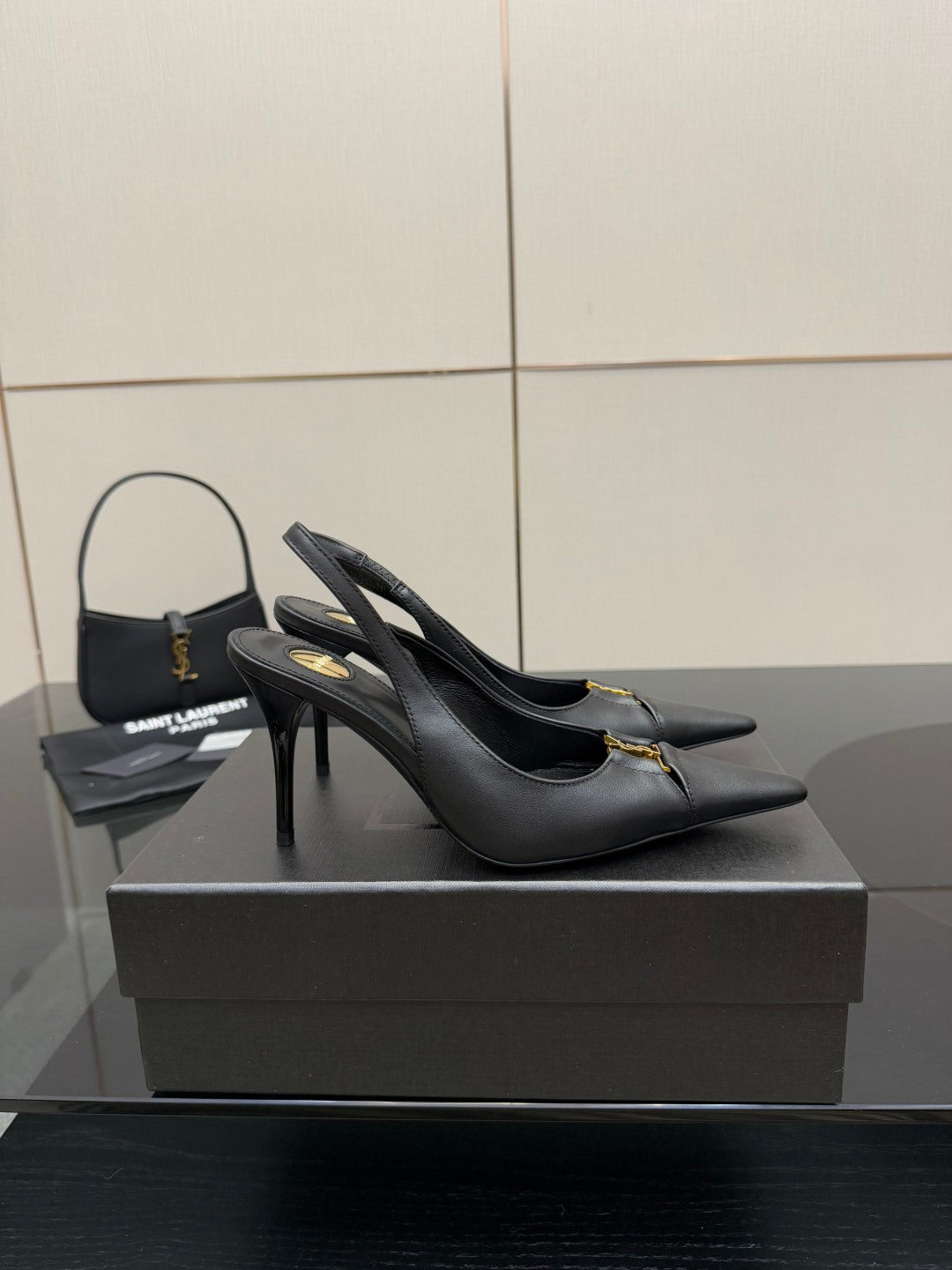 Black slingback stiletto pumps with gold logo detail, angled view on display.