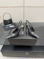 Black pointed-toe stiletto pumps with gold logo detail, angled pair view on display.
