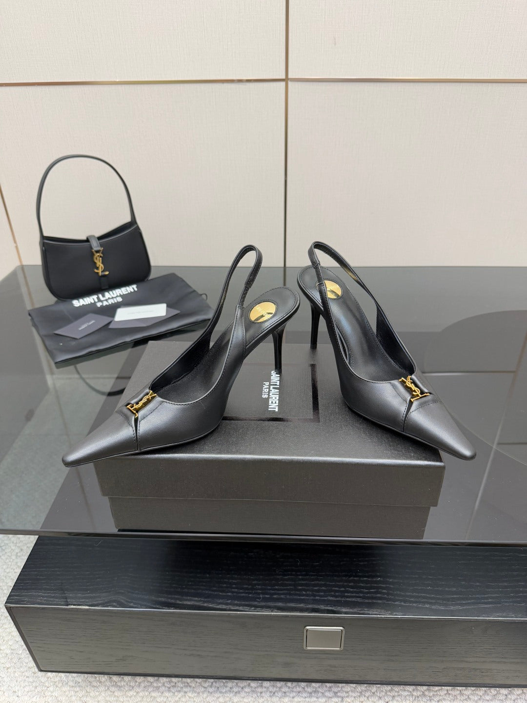Black pointed-toe stiletto pumps with gold logo detail, angled pair view on display.