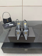 Black pointed-toe stiletto pumps with gold logo detail, on display.
