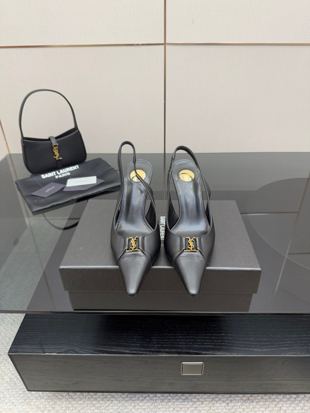 Black pointed-toe stiletto pumps with gold logo detail, on display.