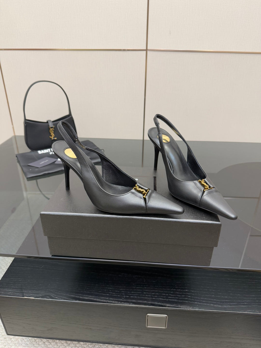 Black pointed-toe stiletto pumps with gold logo detail, front view on display.