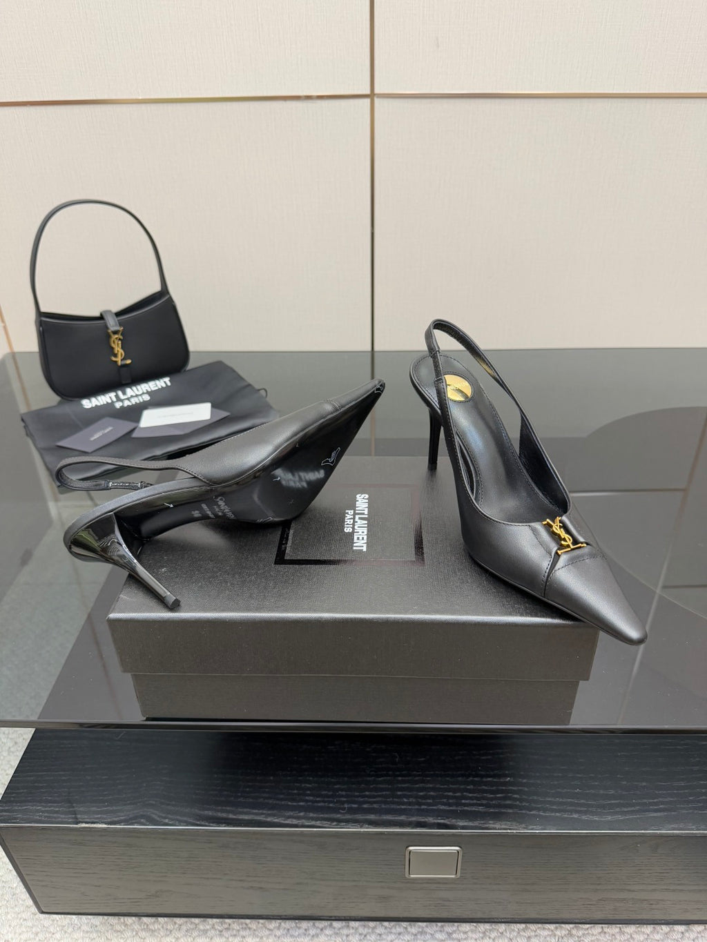 Black pointed-toe stiletto pumps with gold logo trim, heel and toe view on display.