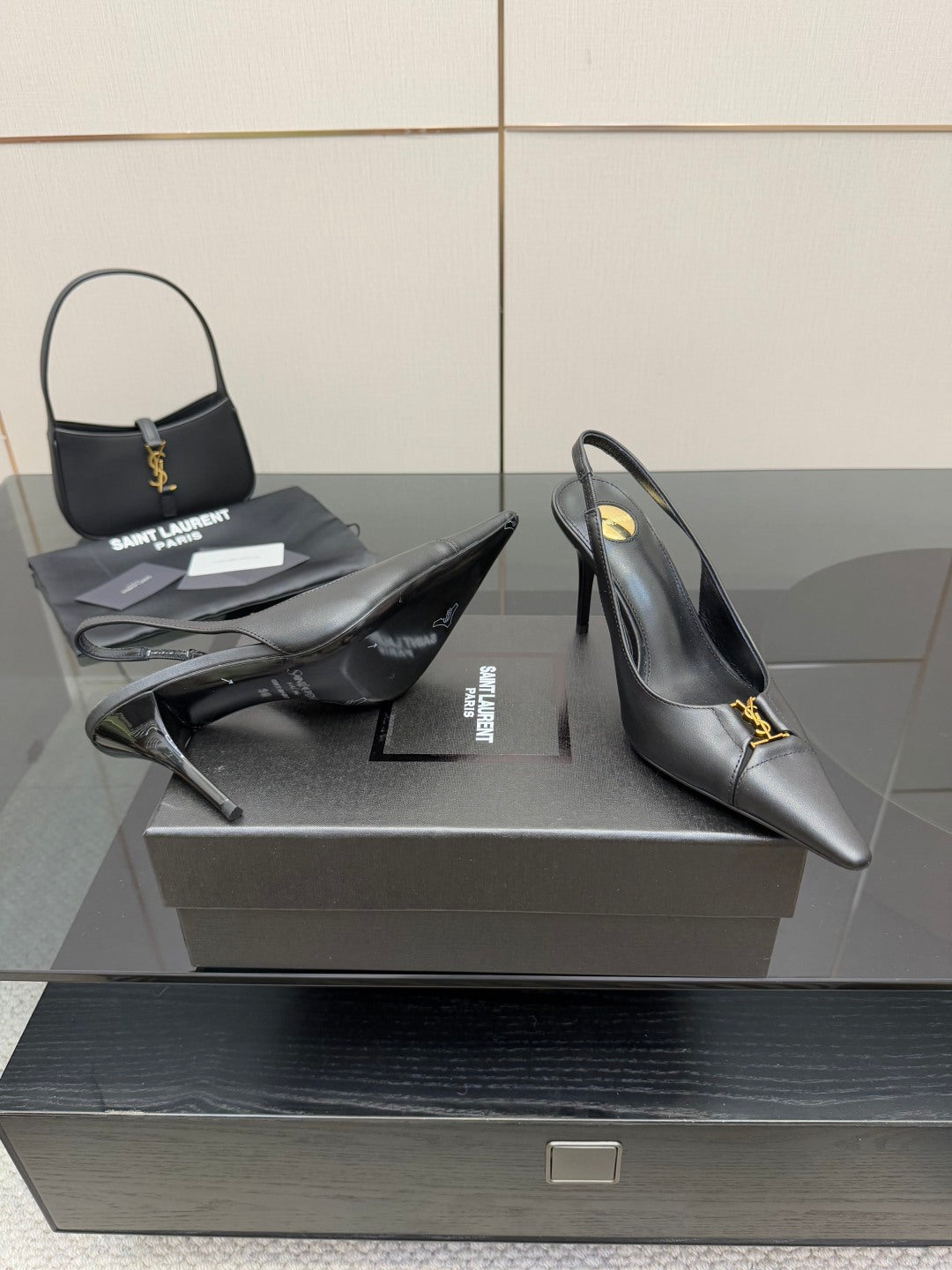Black pointed-toe stiletto pumps with gold logo trim, heel and toe view on display.
