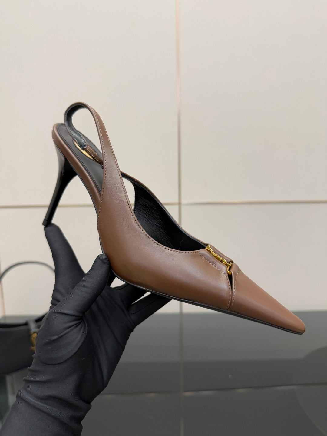 Brown pump held by gloved hand: pointed toe, slingback strap, high heel