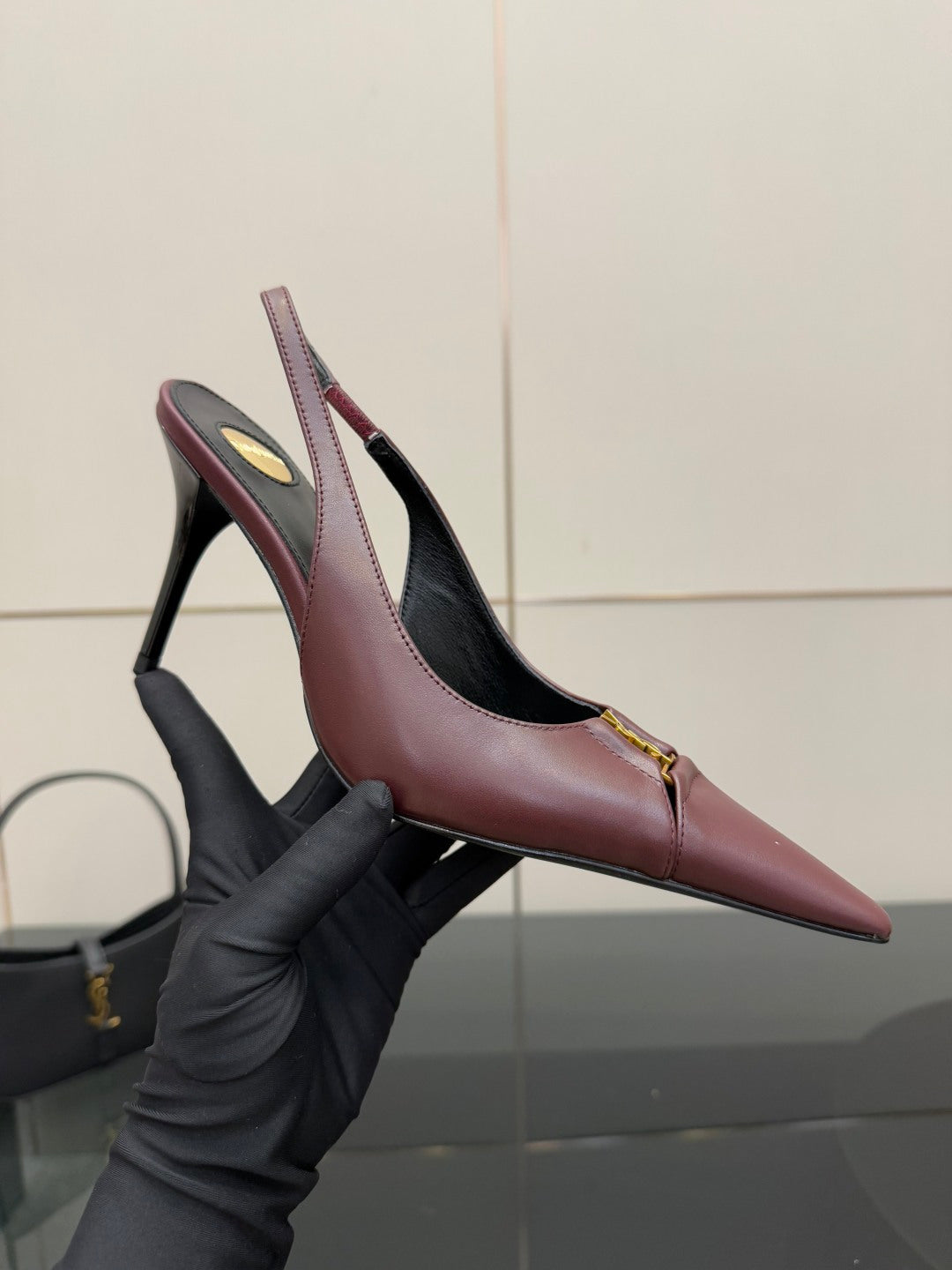 Burgundy pointed-toe slingback heel shown in gloved hand, gold logo detail