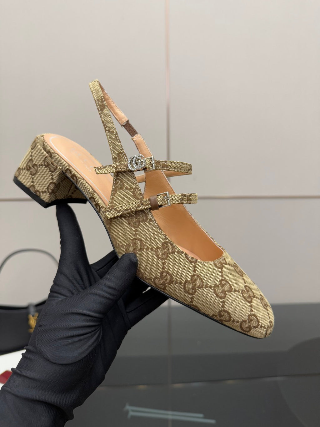 Gucci GG-pattern slingback mule held up, showing crisscross strap with hardware