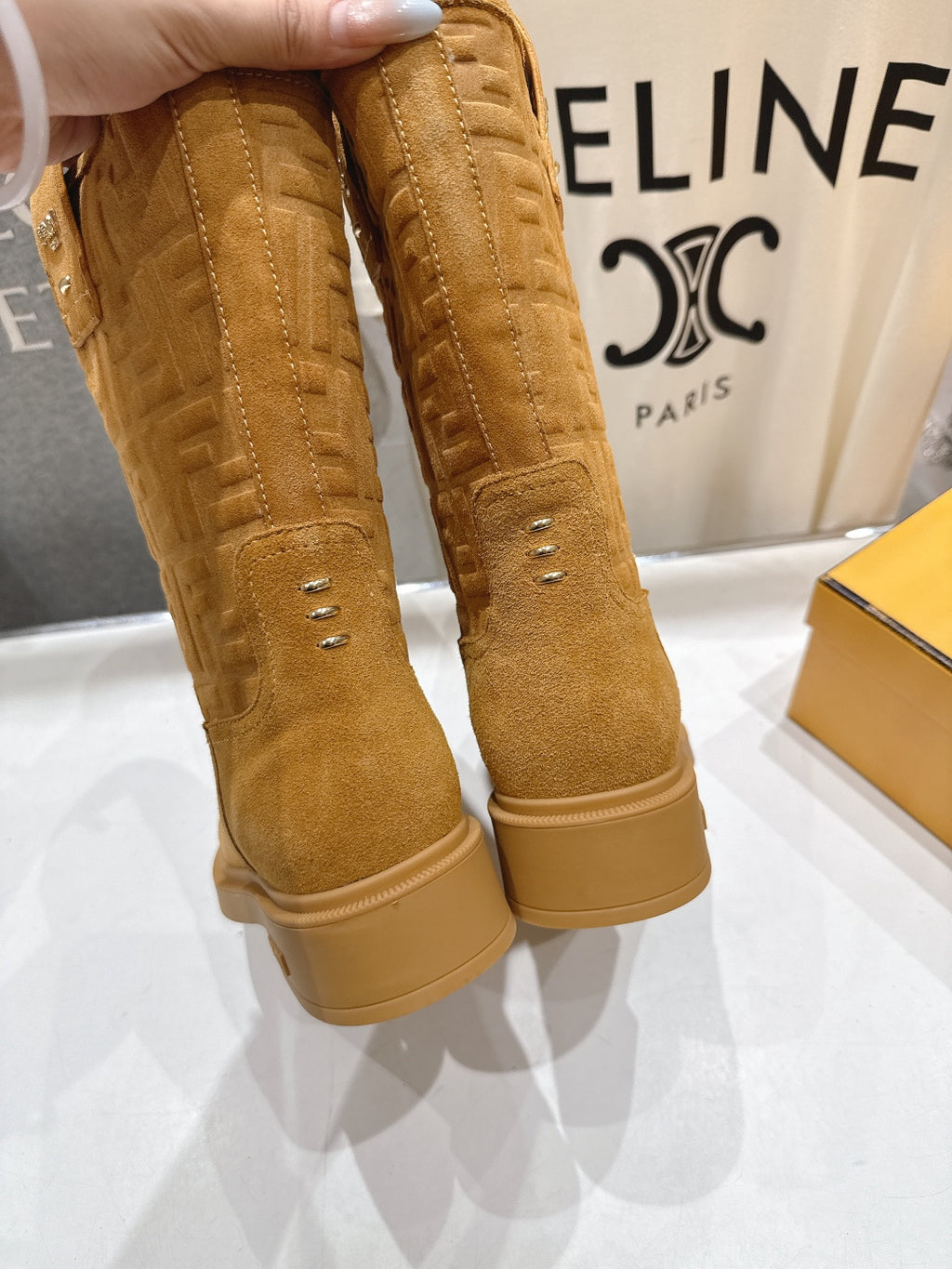 Tan suede ankle boots held by hand, showing stitched seams and pull tabs