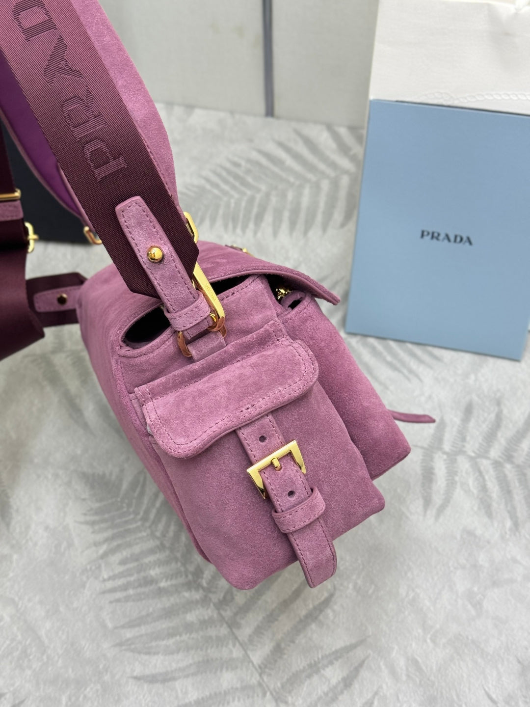 Purple suede strap with gold-tone buckle hardware and front flap tab on shoulder bag