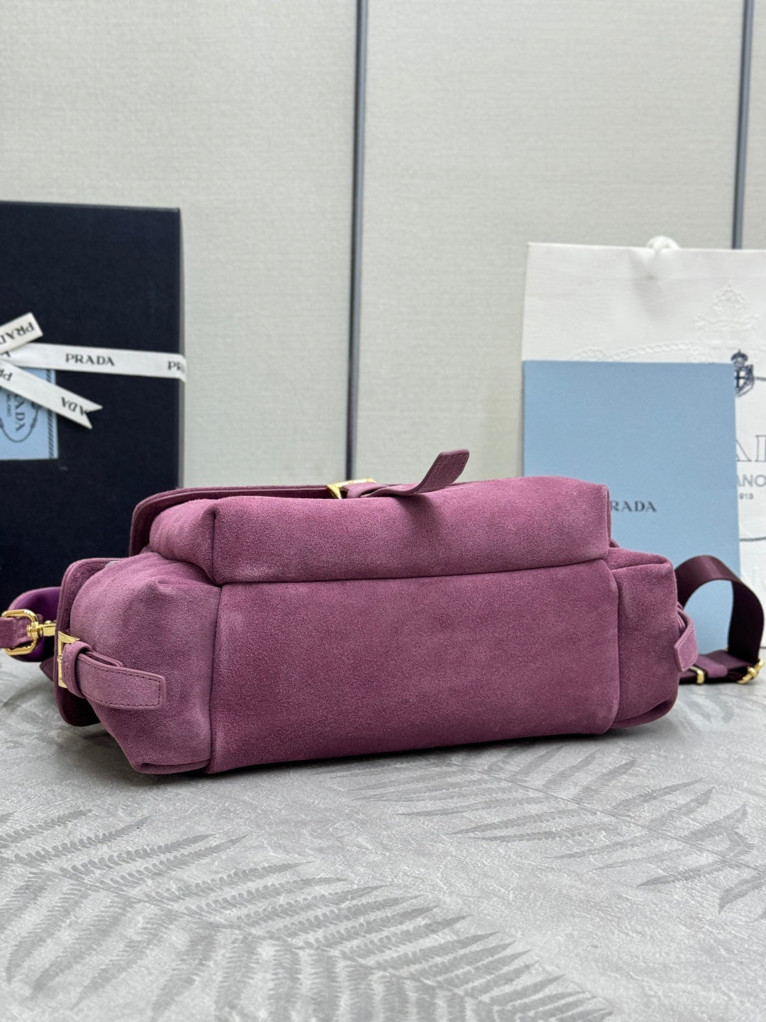 Purple suede handbag with rolled top, stacked straps, and gold-tone hardware accents