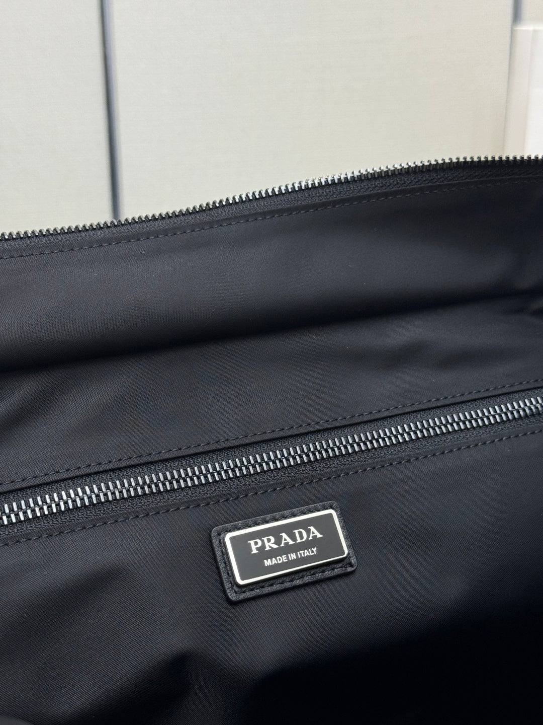 Black Prada nylon bag close-up of silver PRADA logo plate and double zipper