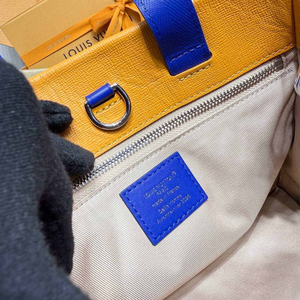 Textured leather bag with blue strap, silver zipper, and blue logo patch
