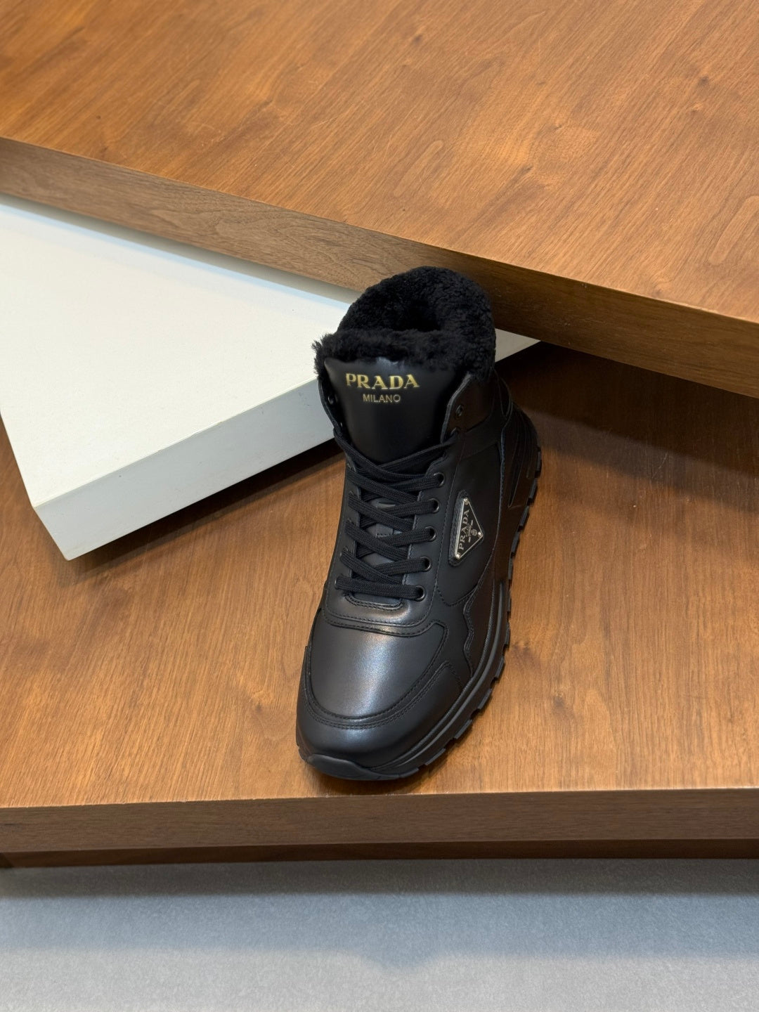 Prada dark winter sneaker on a shelf, featuring shearling trim and lace-up front