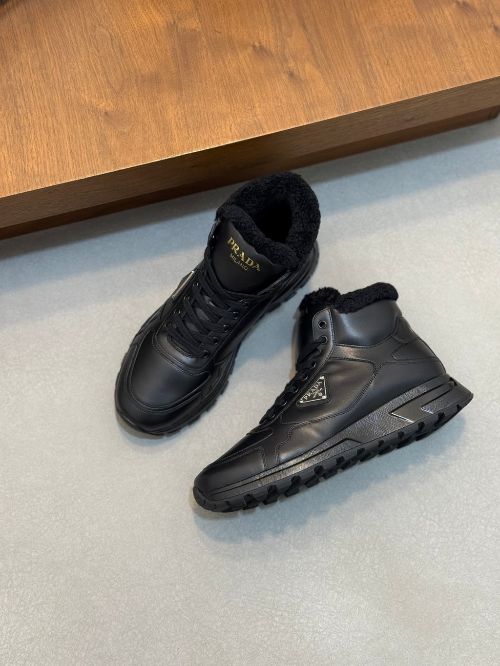 Two Prada dark leather winter sneakers, one side view showing shearling collar and tread sole
