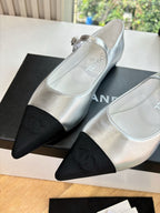 Women’s Chanel silver flats with black toe cap and bow detail across strap