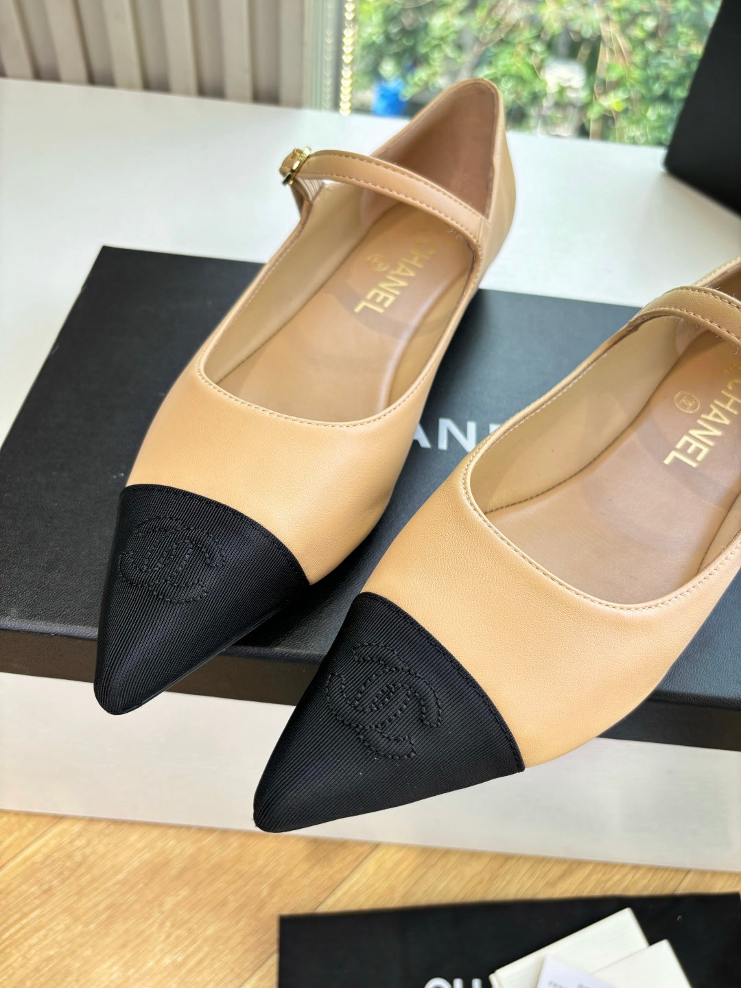 Beige flats with pointed toe, black toe caps, and ankle strap detail