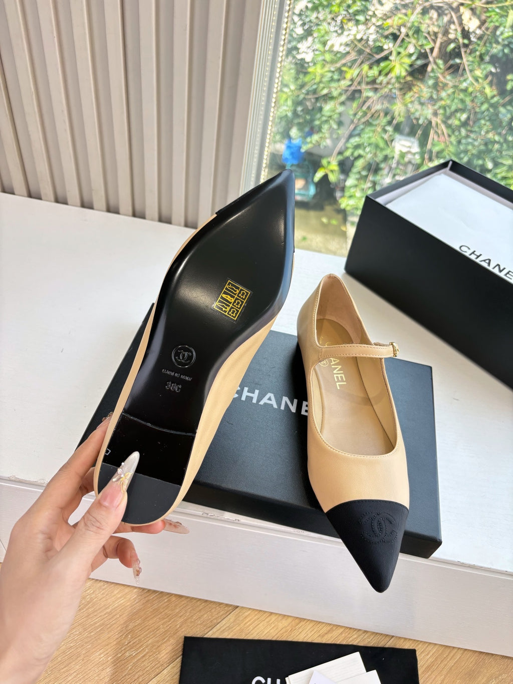 Two-tone flat shoe side view with gold-toned details, beige upper and black sole
