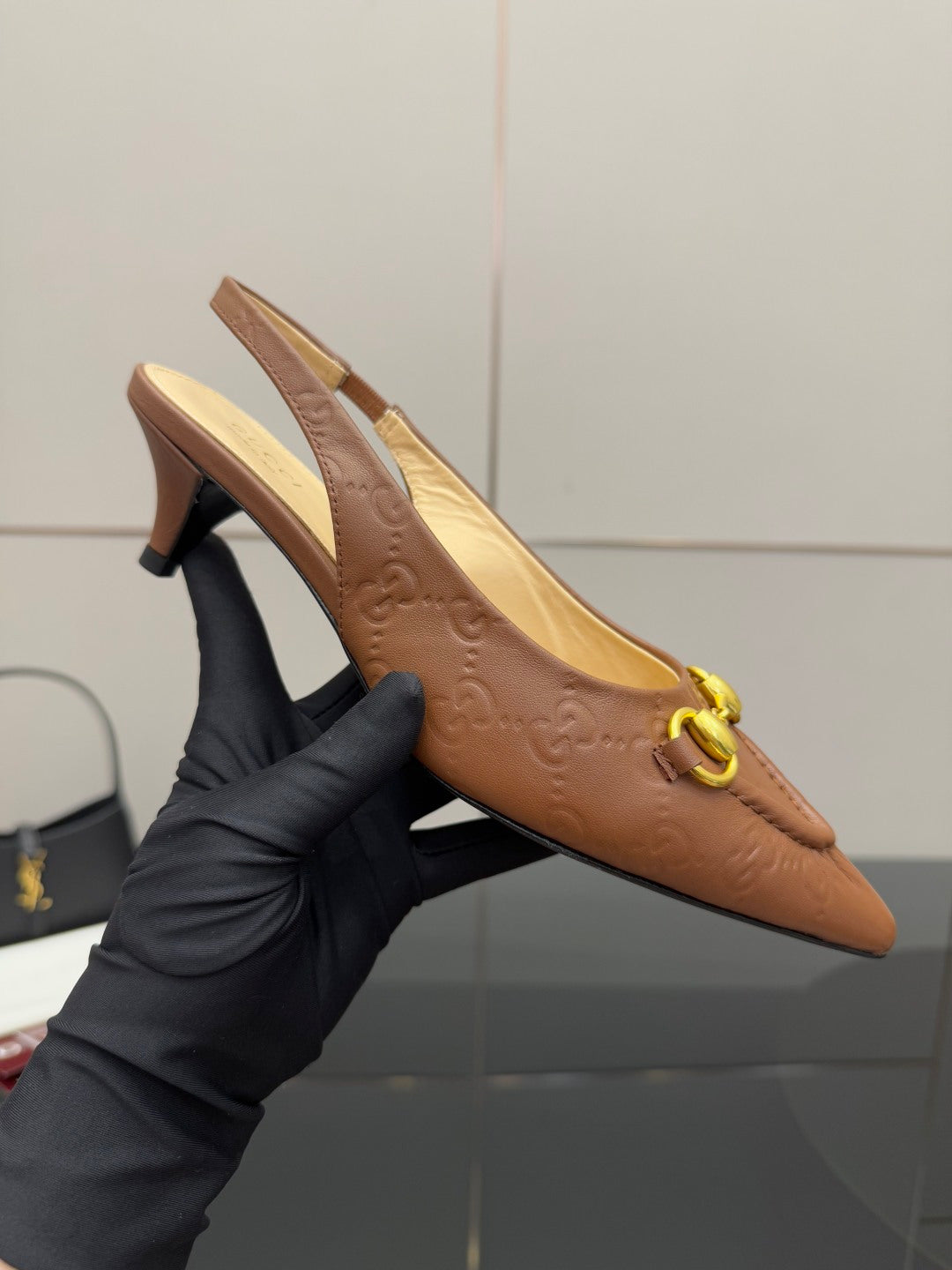 Brown slingback heel held in hand with gold ring detail and pointed toe
