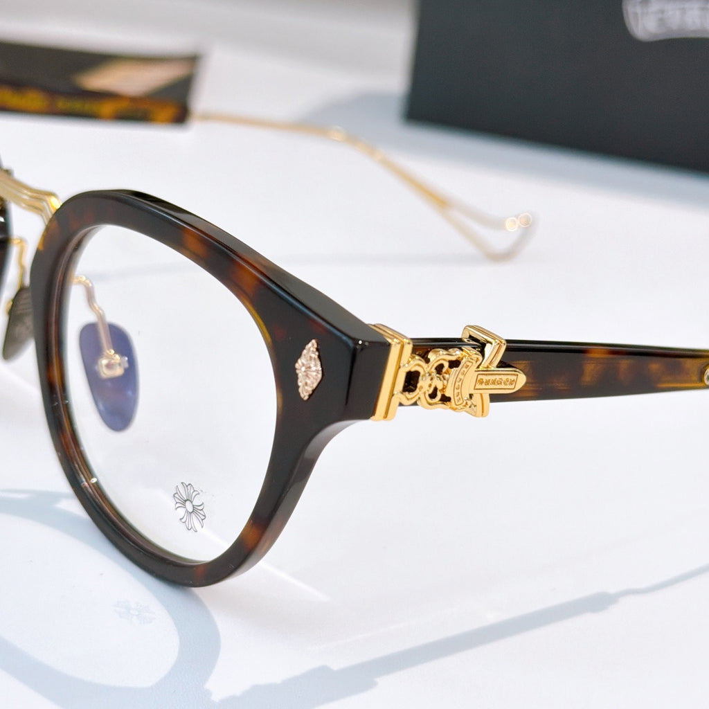 Side view of black round-frame glasses with gold-tone hinge and decorative front detail.
