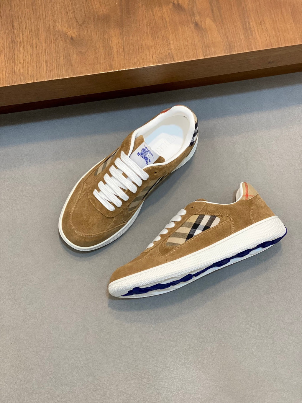 Tan suede sneakers on a display shelf with white laces and blue check detail